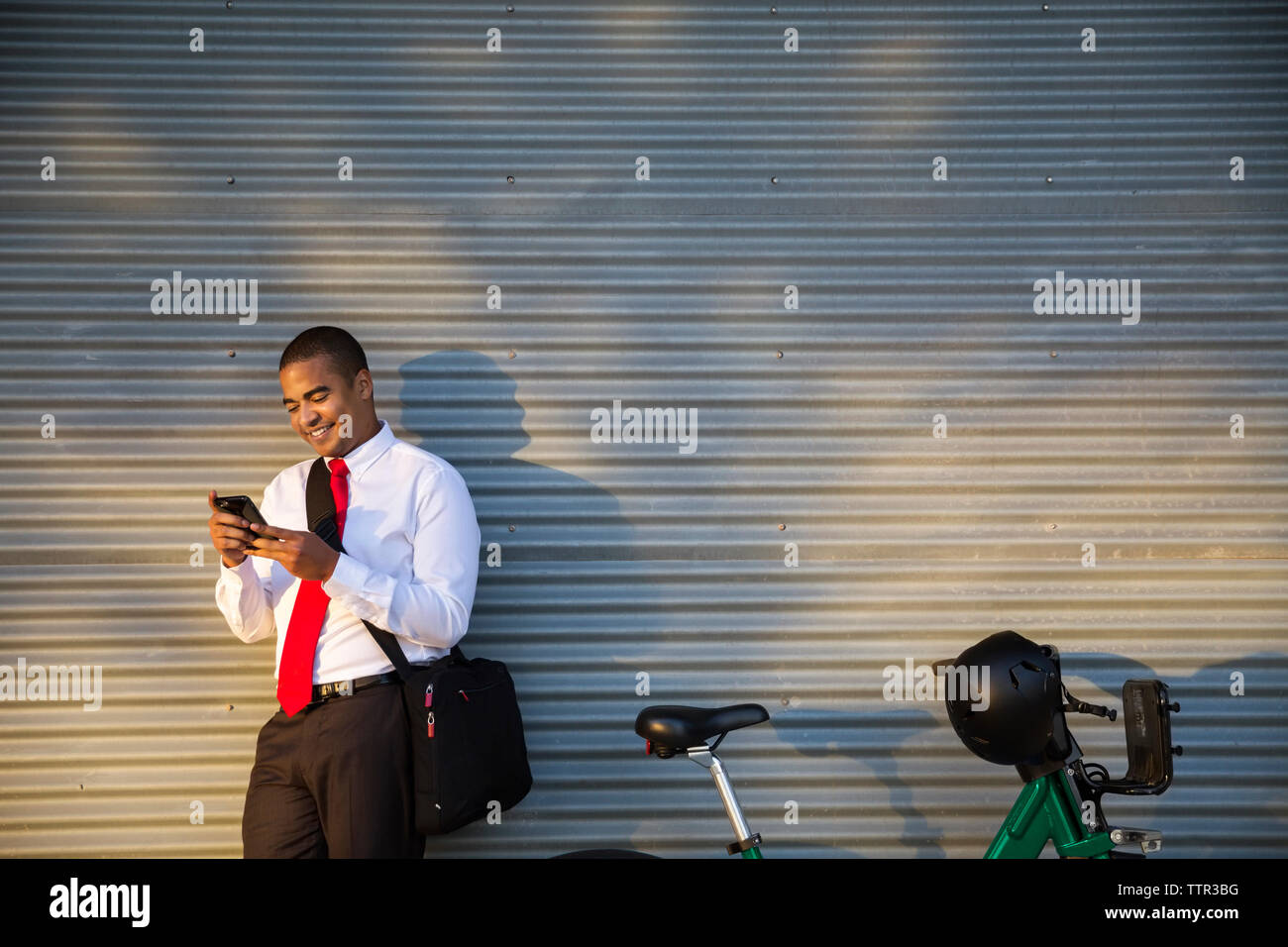 Smiling businessman using mobile phone while standing against closed shutter Stock Photo