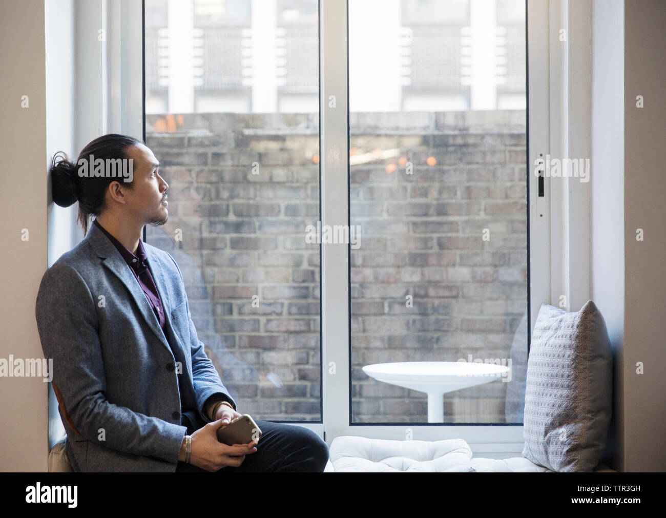 Thoughtful man looking through window while sitting in office Stock Photo