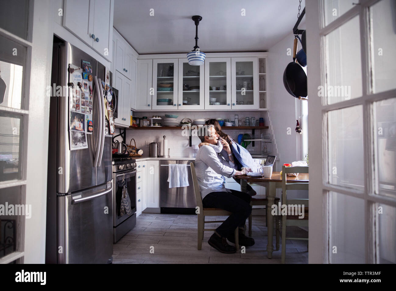 Daughter embracing father using laptop computer in kitchen at home Stock Photo