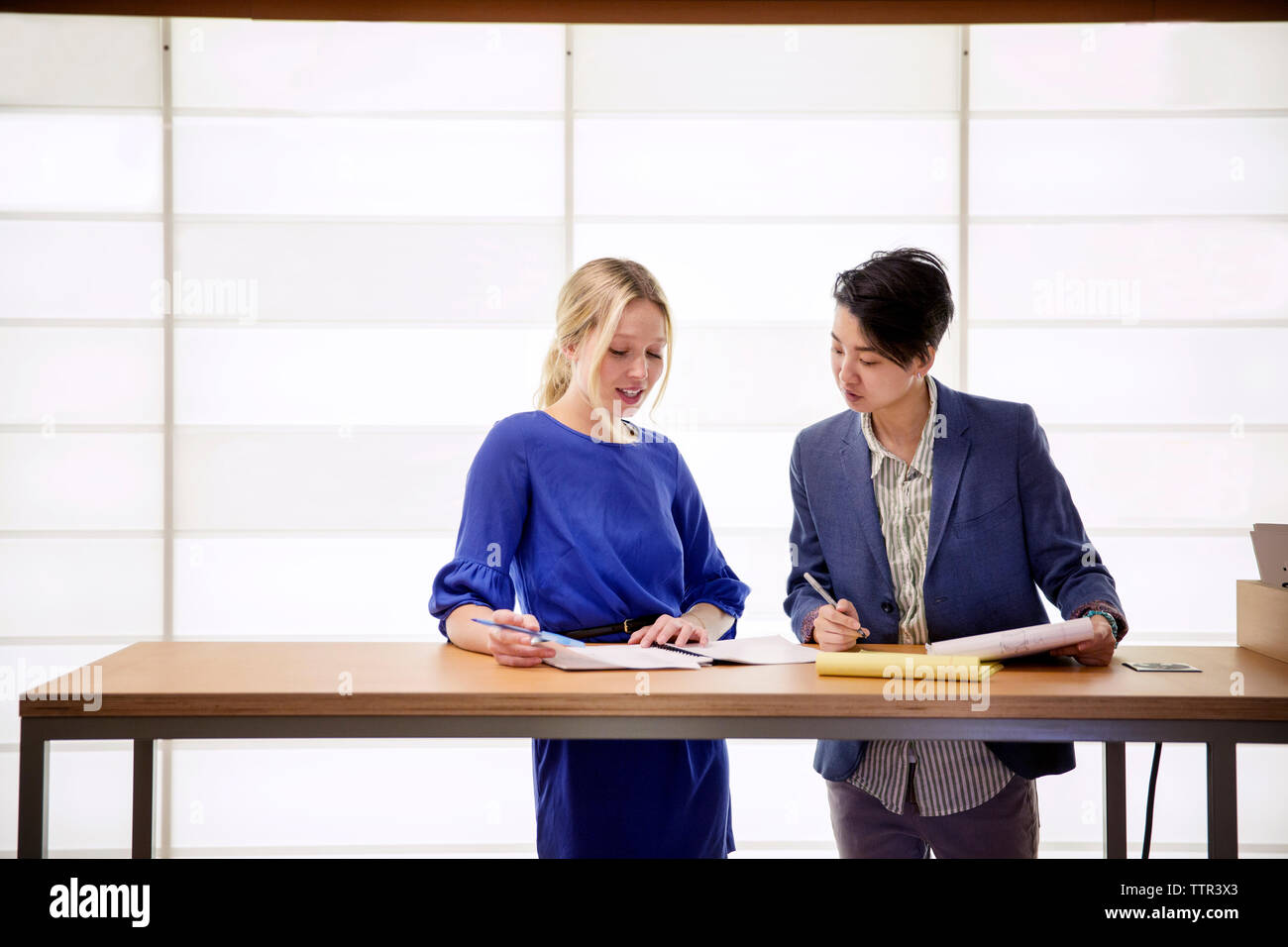 Female colleagues discussing while standing at table in office Stock Photo