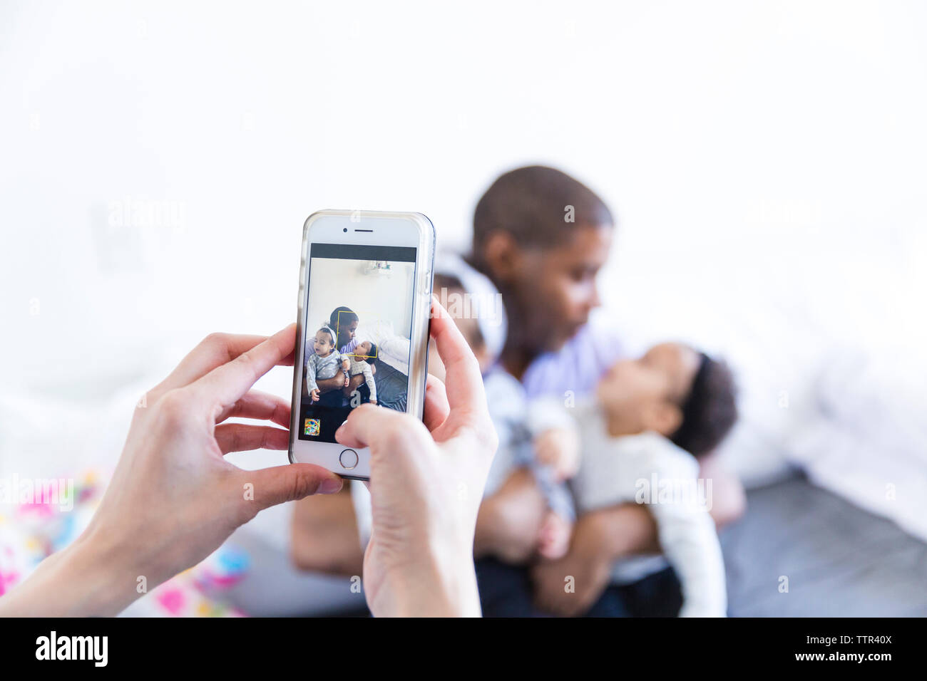 Cropped hands of woman photographing man with baby girls at home Stock Photo