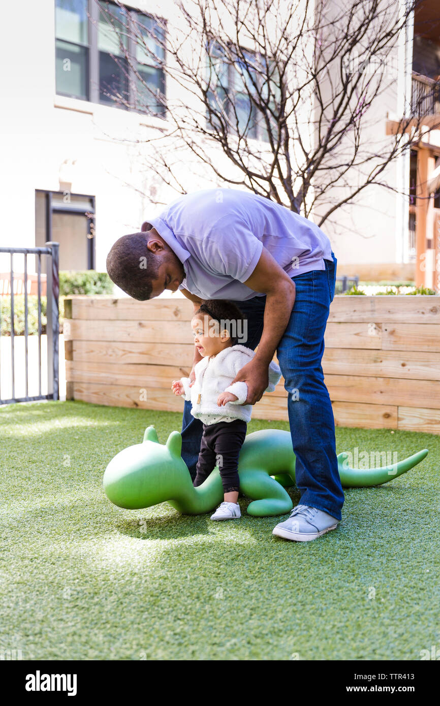 Father holding daughter playing on animal statue at park Stock Photo ...