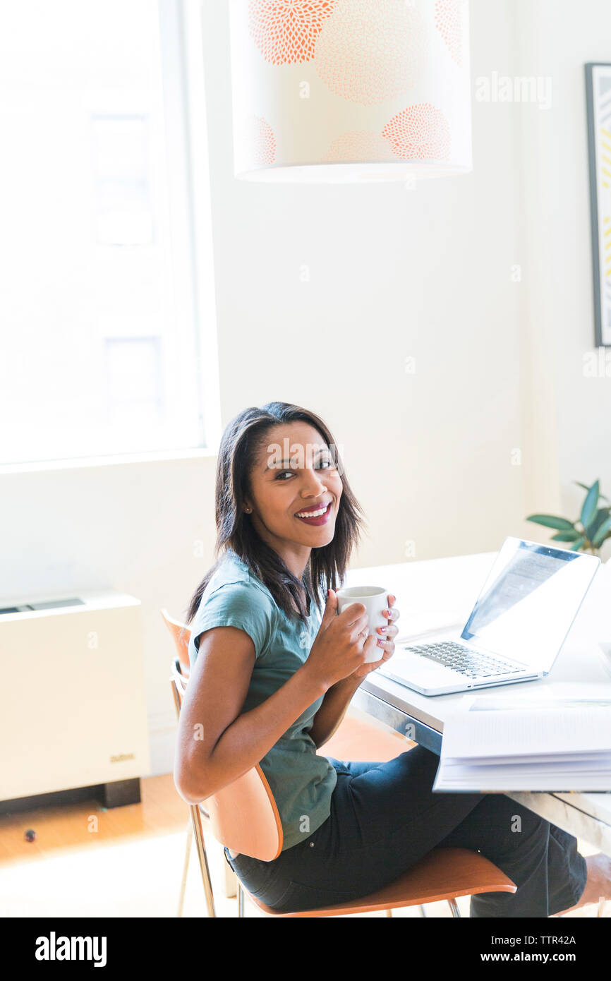 Happy woman having coffee while working at home office Stock Photo