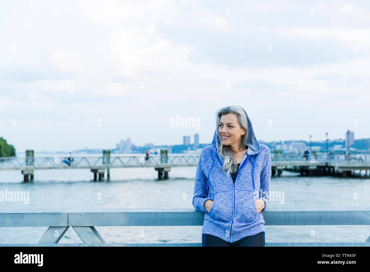Woman with hands in pockets looking away while standing on bridge Stock ...