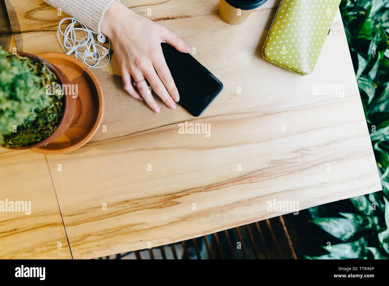Cropped hand of young woman holding smart phone on wooden table at cafe Stock Photo