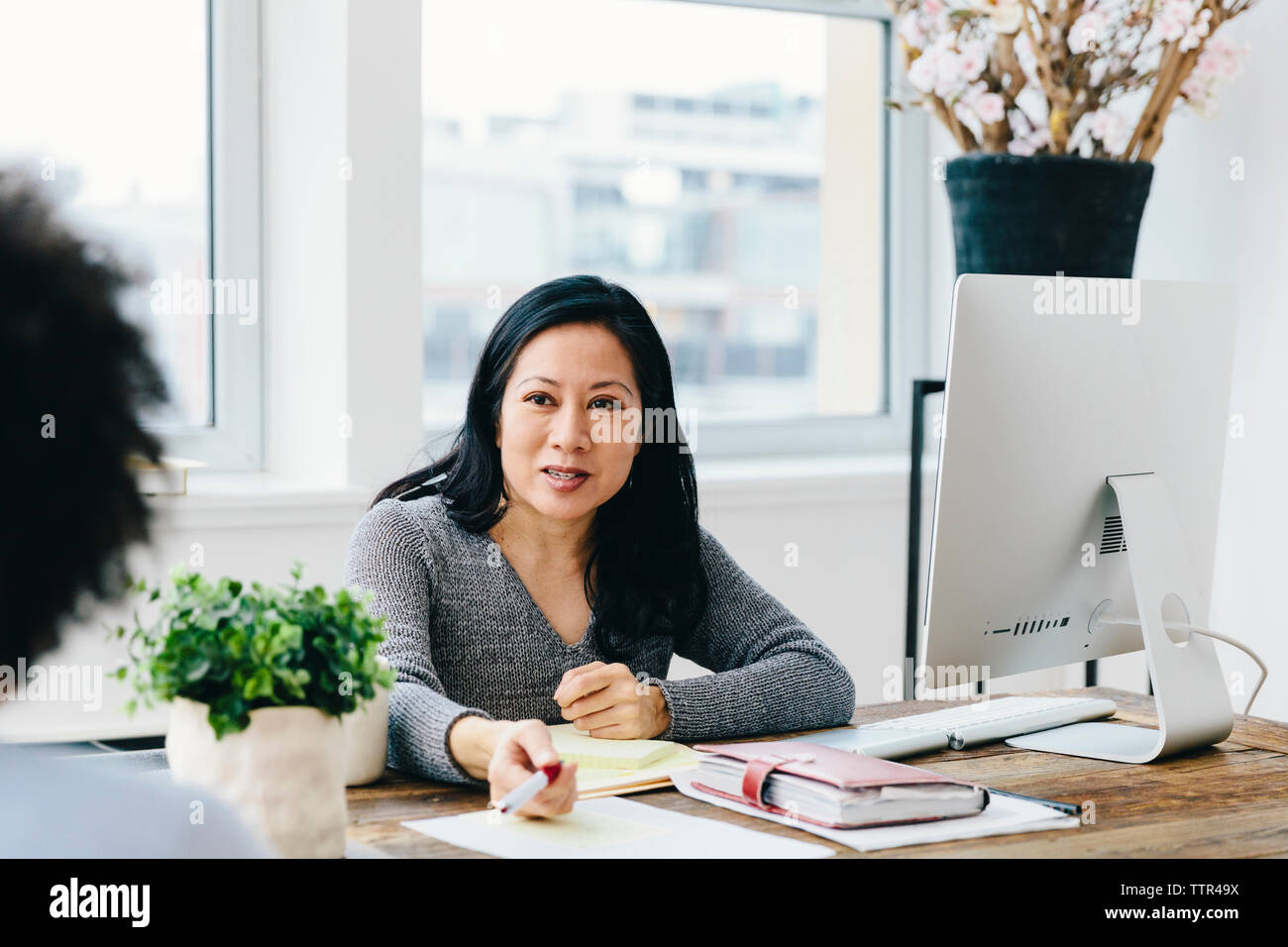 businesswoman talking with female colleague while working at desk in office Stock Photo