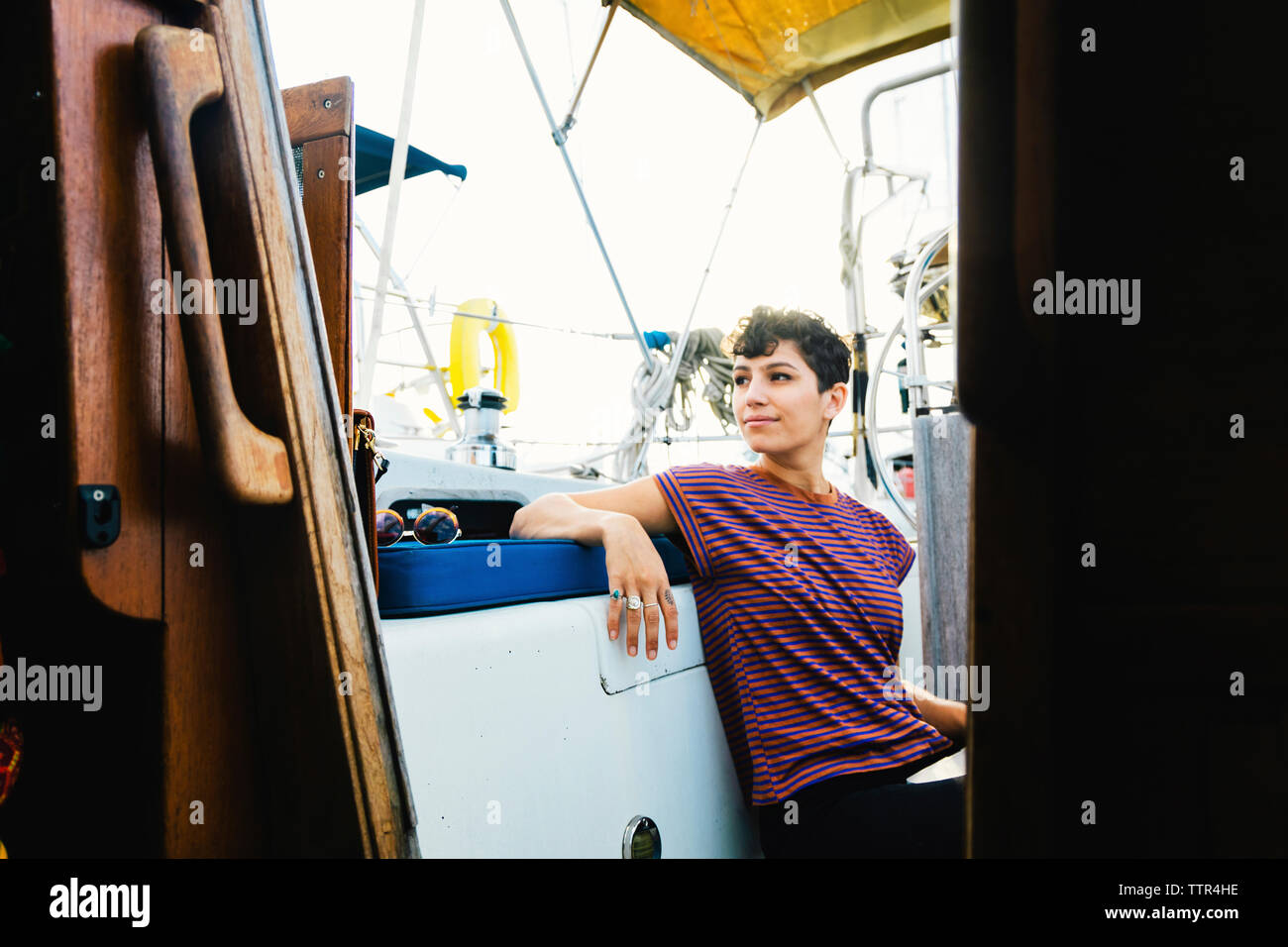 Thoughtful woman looking away while sitting in boat against sky seen through window Stock Photo