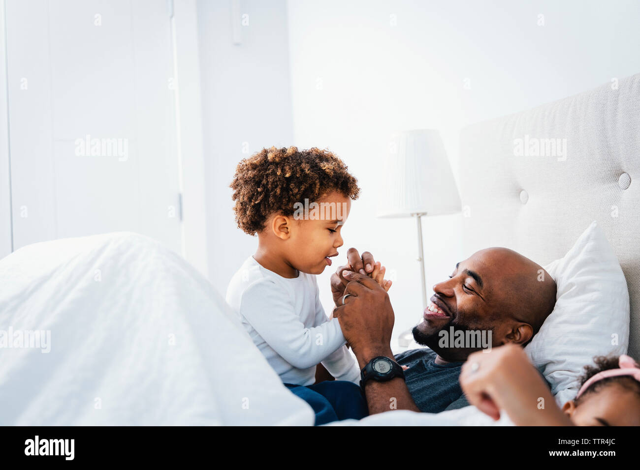 Happy father playing with son while relaxing on bed against wall at home Stock Photo
