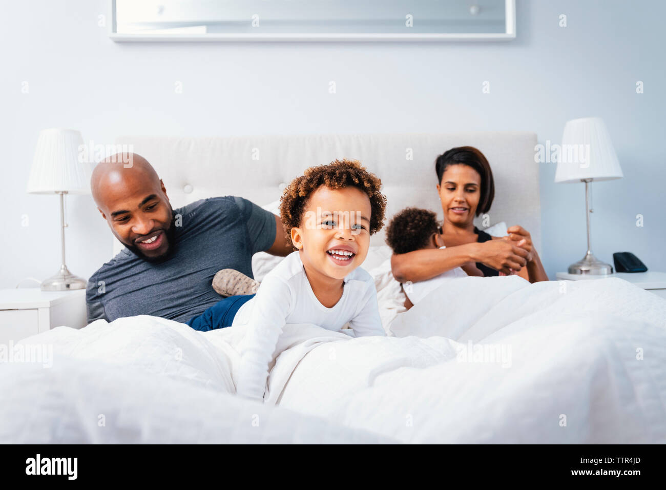 Parents playing with children while relaxing on bed against wall at home Stock Photo