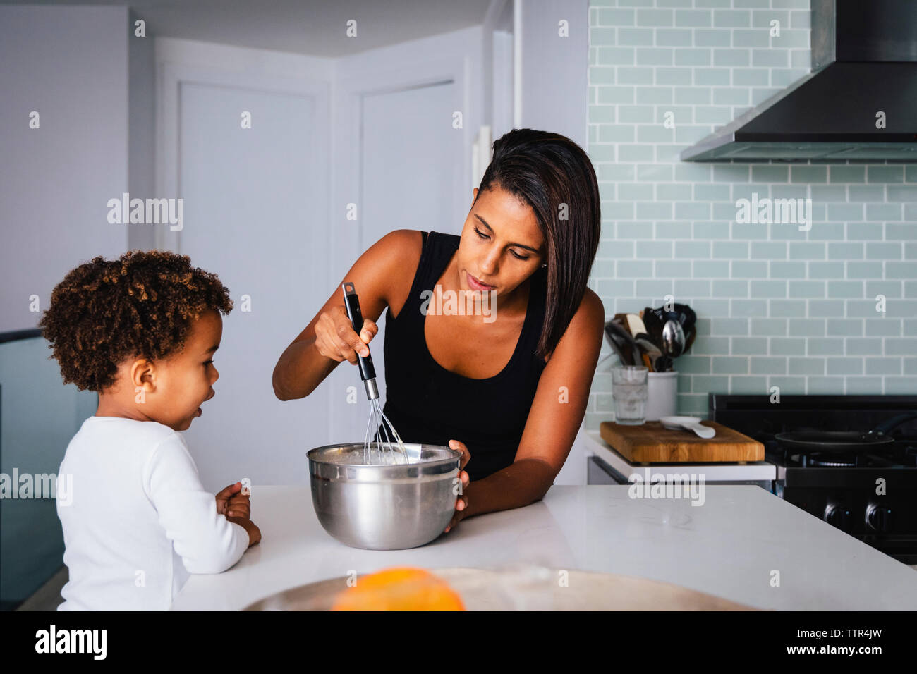 Son looking at mother preparing food on kitchen island Stock Photo