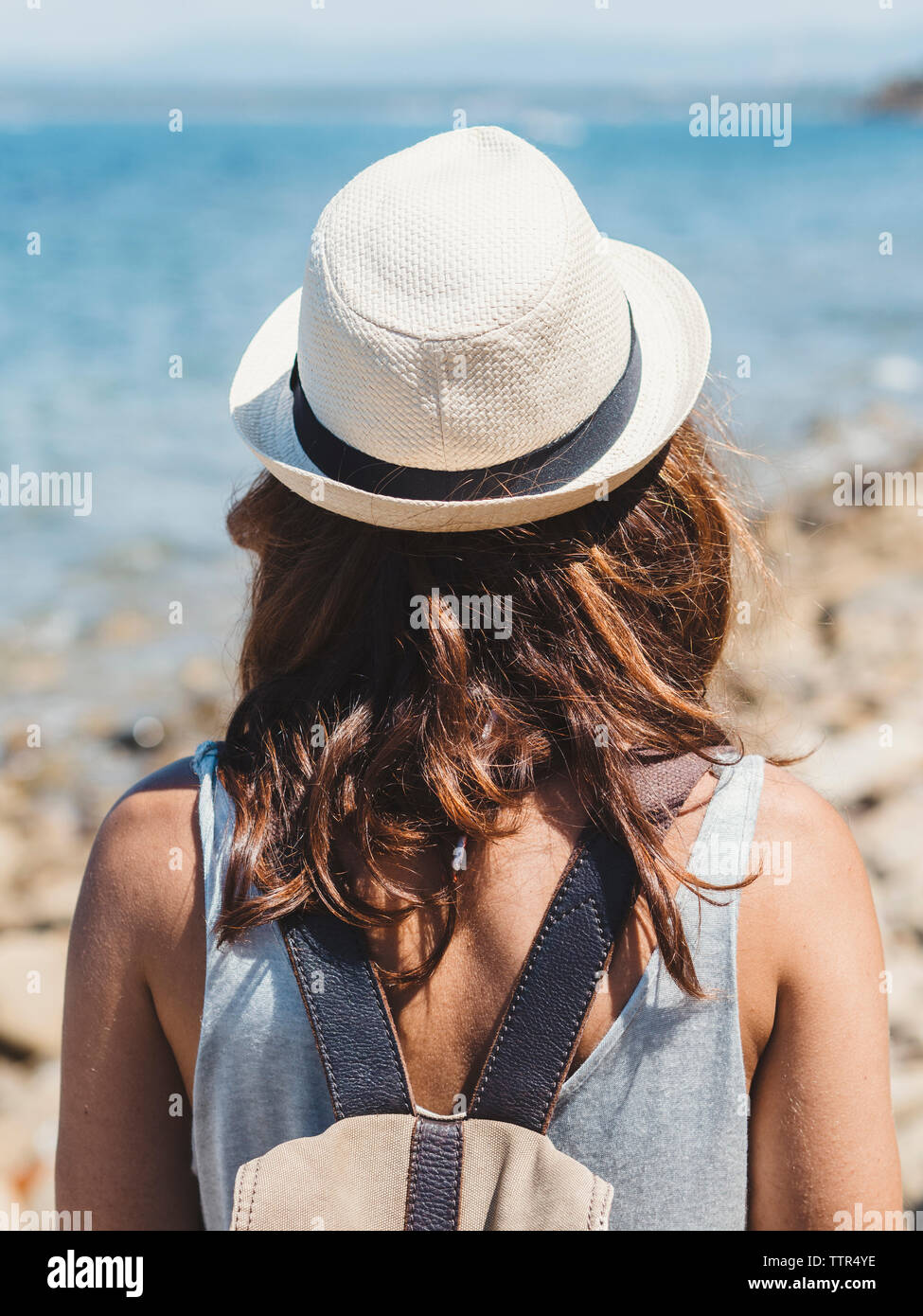 Rear view of woman with backpack looking at view while standing on rocky beach during sunny day Stock Photo