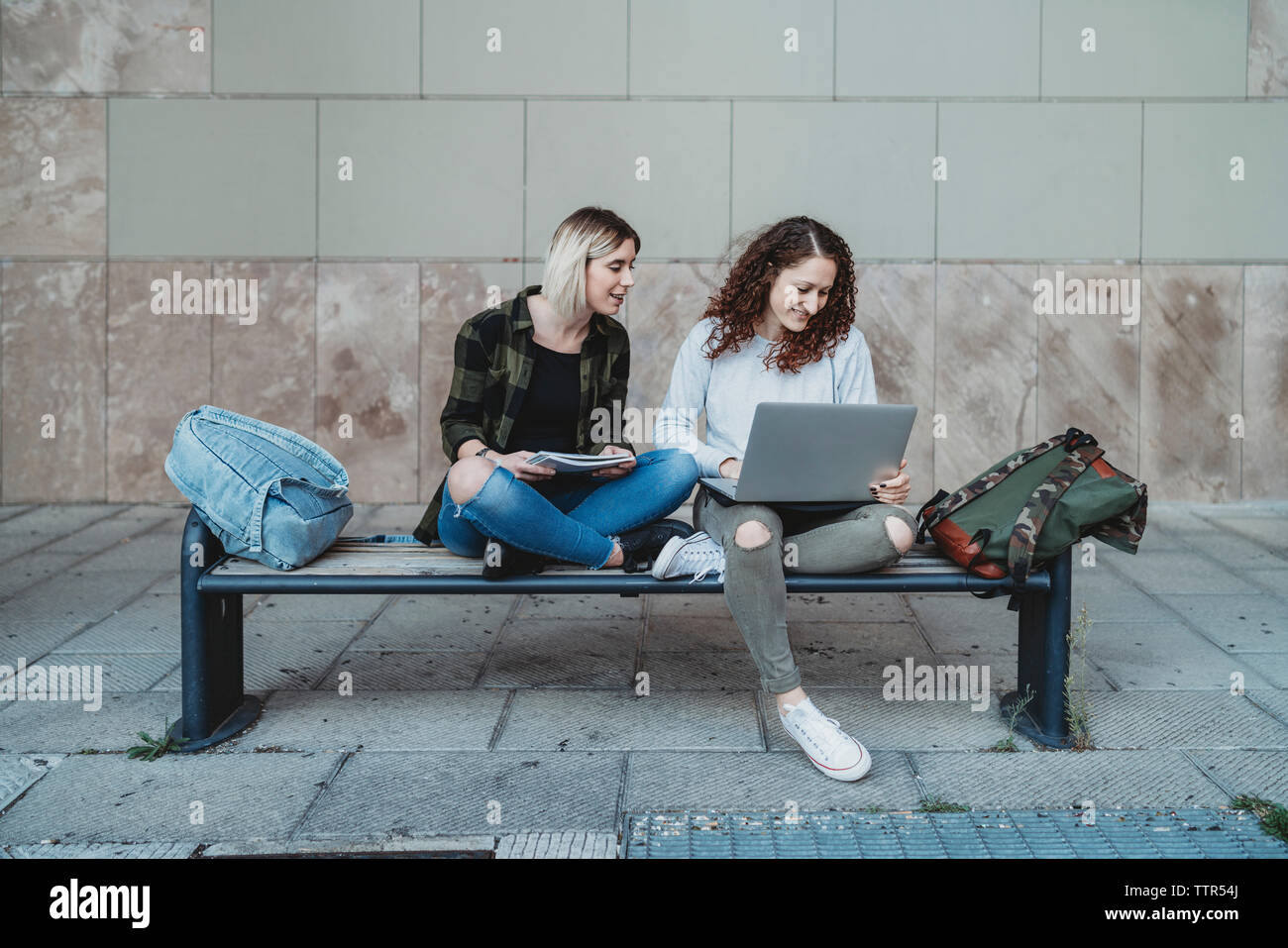 Two young women studying using laptop on the bench Stock Photo - Alamy