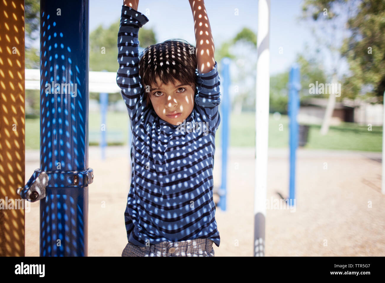 Portrait of boy hanging from outdoor play equipment at playground Stock Photo