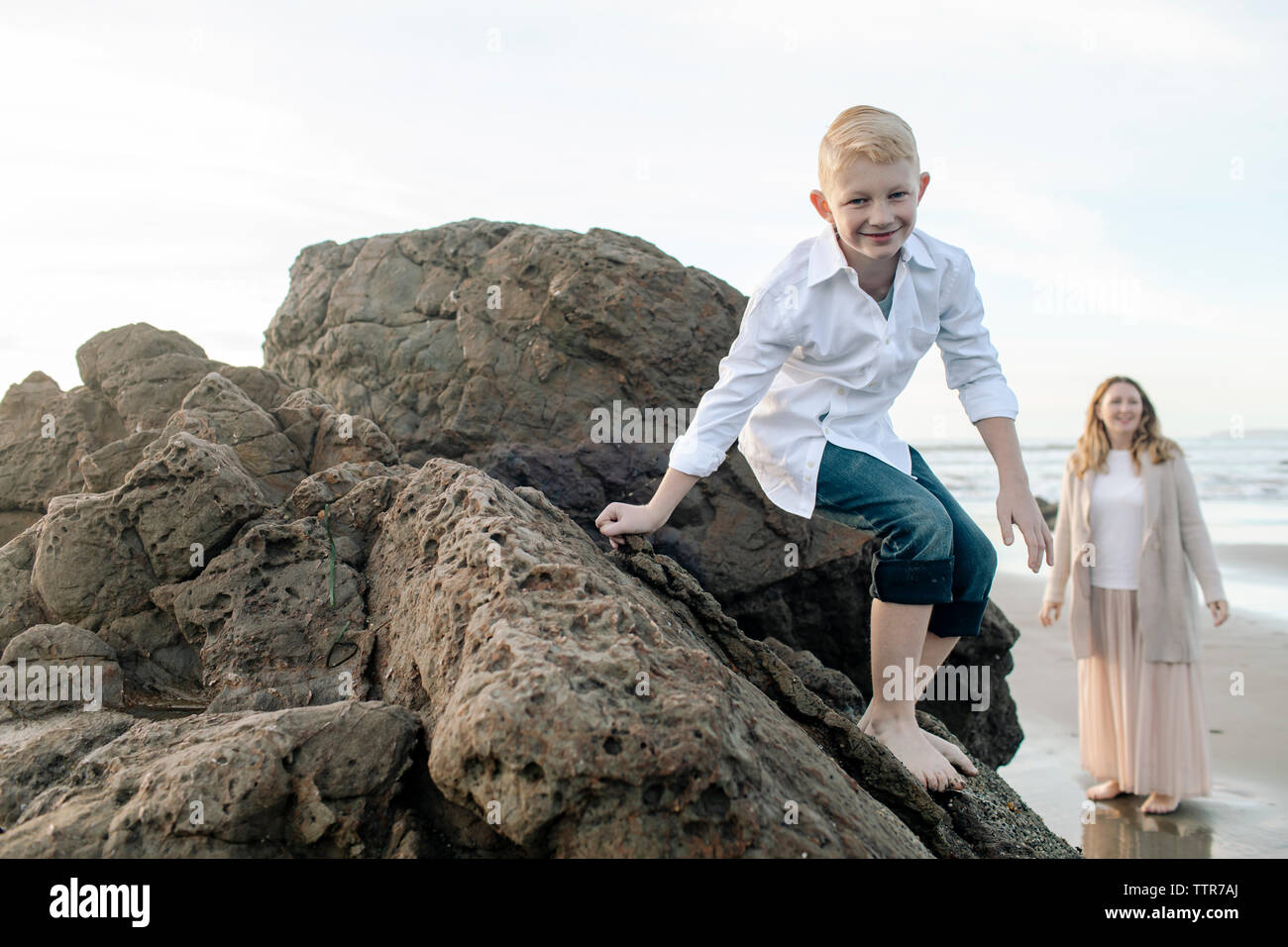 Son climbing down a rock at the beach Stock Photo