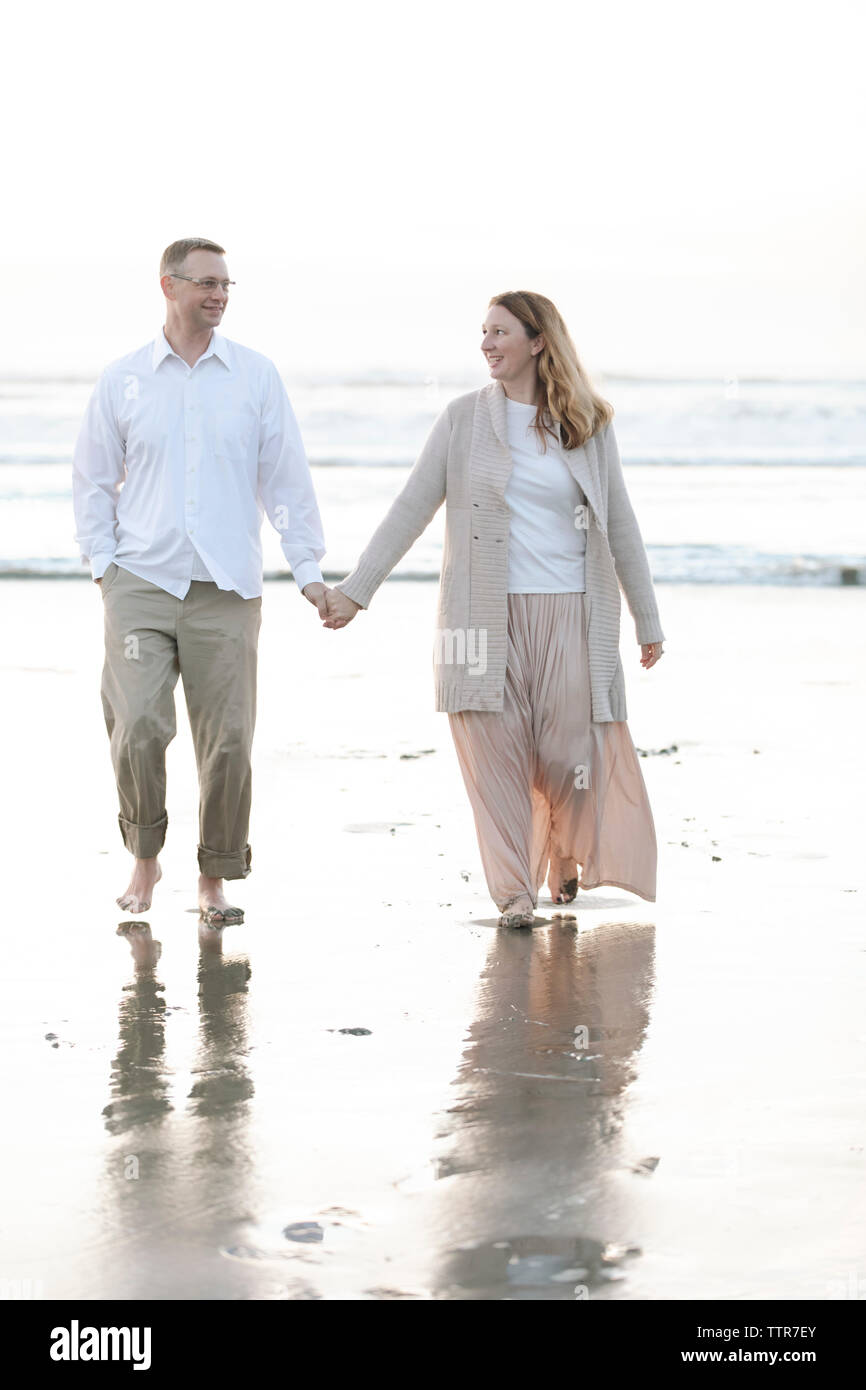 Mid-age couple walking toward on beach against clear sky Stock Photo