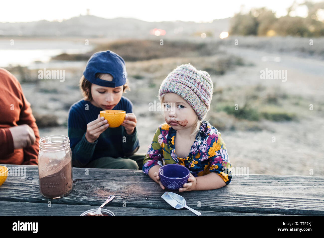Adorable girl with brother drinking hot cocoa by woodden table at twilights Stock Photo