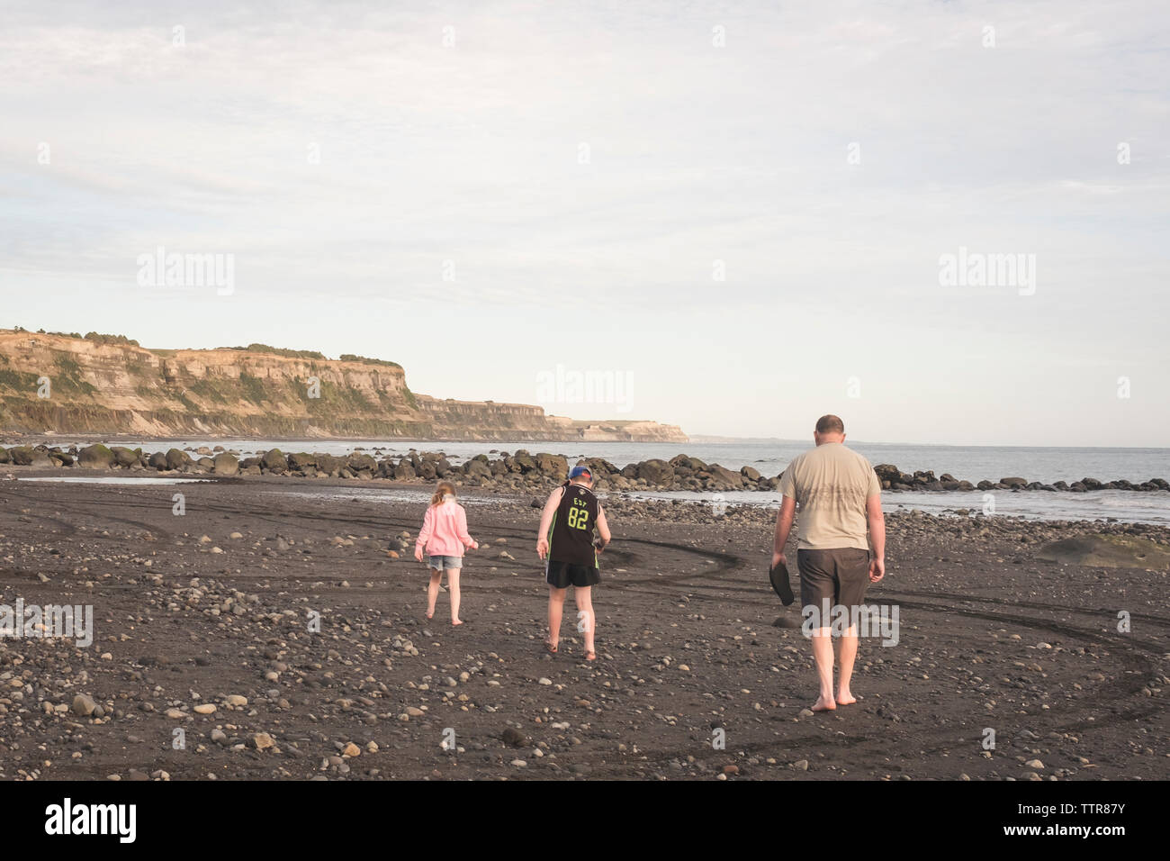 Family walking across black sand beach with cliffs in the background Stock Photo