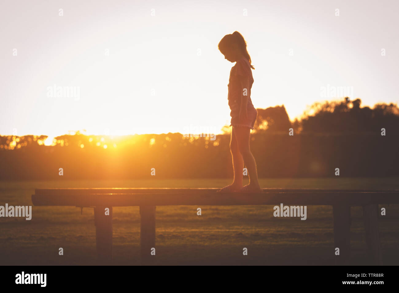Side view of young girl walking on playground equipment at sunset Stock Photo