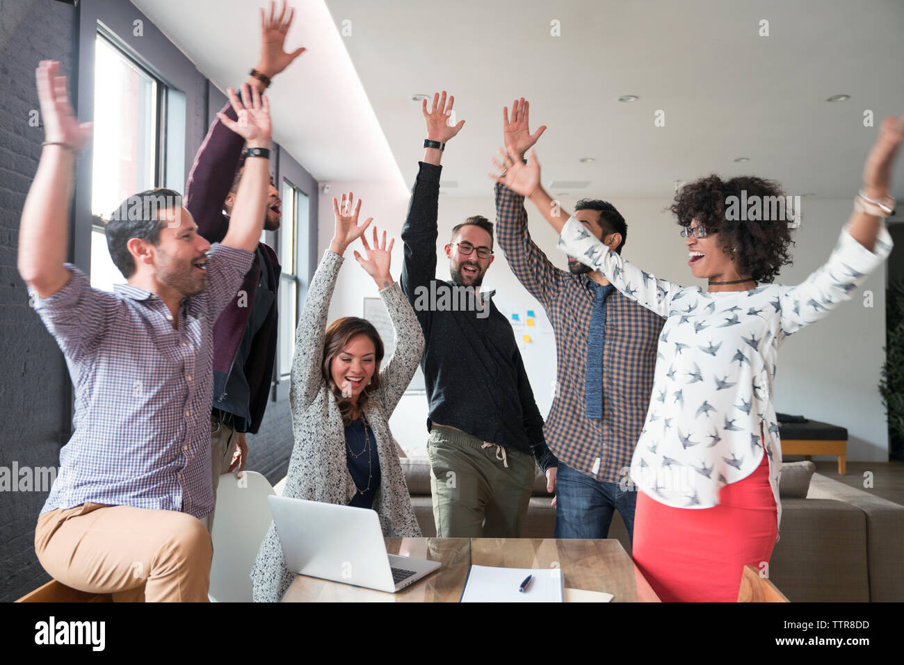 Happy business people with arms raised at desk in office Stock Photo