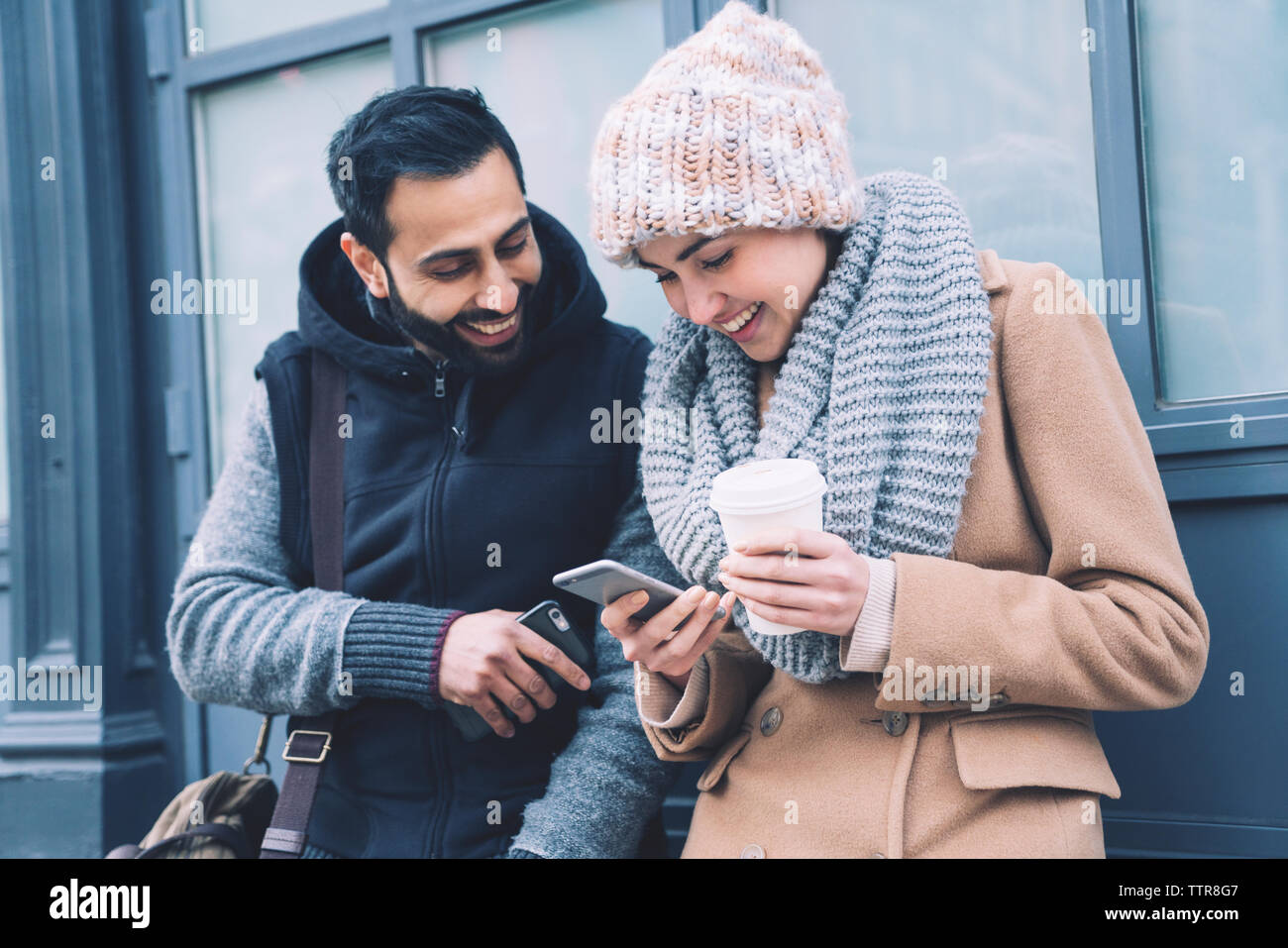 Happy couple using mobile phone while leaning by building in city Stock Photo