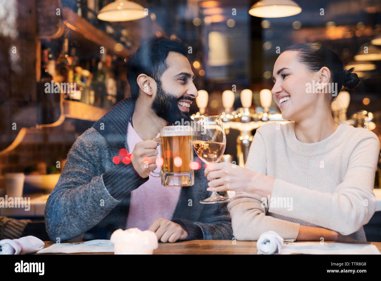 Happy couple toasting drinks seen through restaurant window Stock Photo