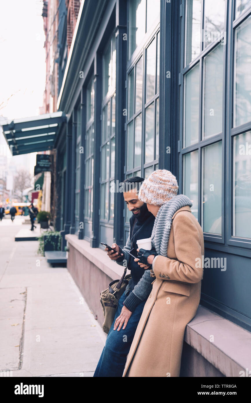 Couple using mobile phone while leaning by building in city Stock Photo