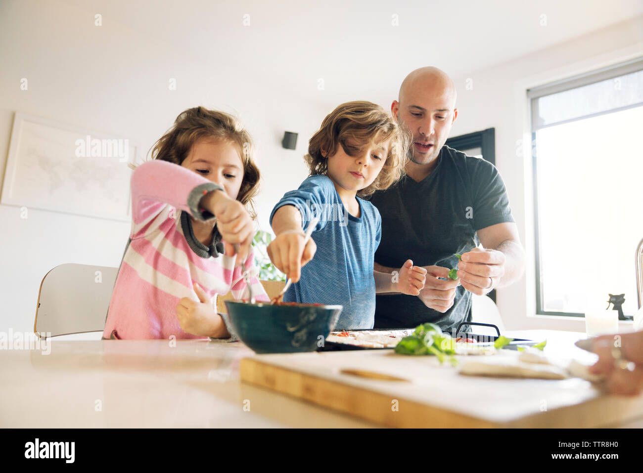 Father assisting son and daughter in preparing food at home Stock Photo