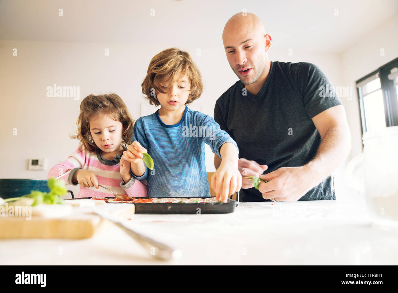 Father preparing food with children at table in home Stock Photo