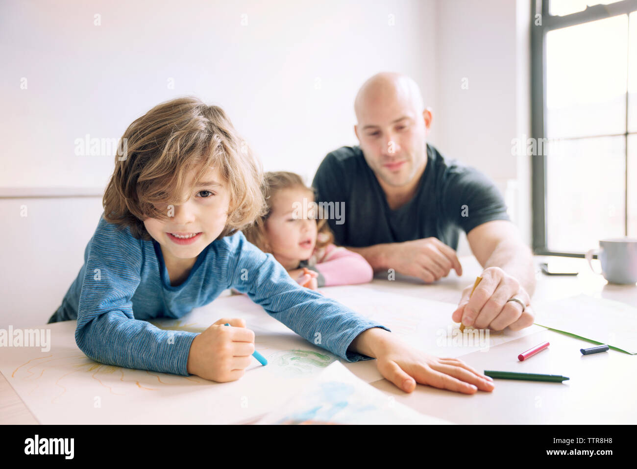 Portrait of boy drawing while father assisting daughter at table in home Stock Photo