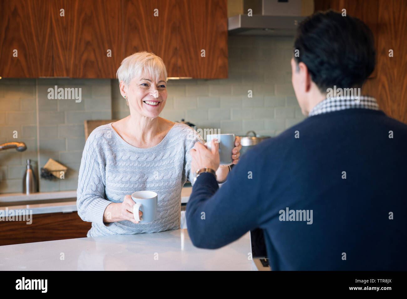 Smiling woman giving mug to man while sitting at table in home Stock Photo