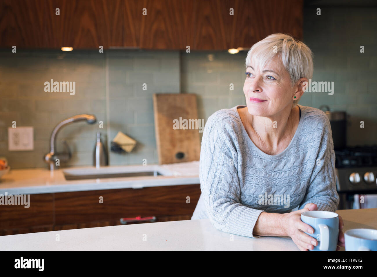 Thoughtful senior woman looking away while leaning on table Stock Photo