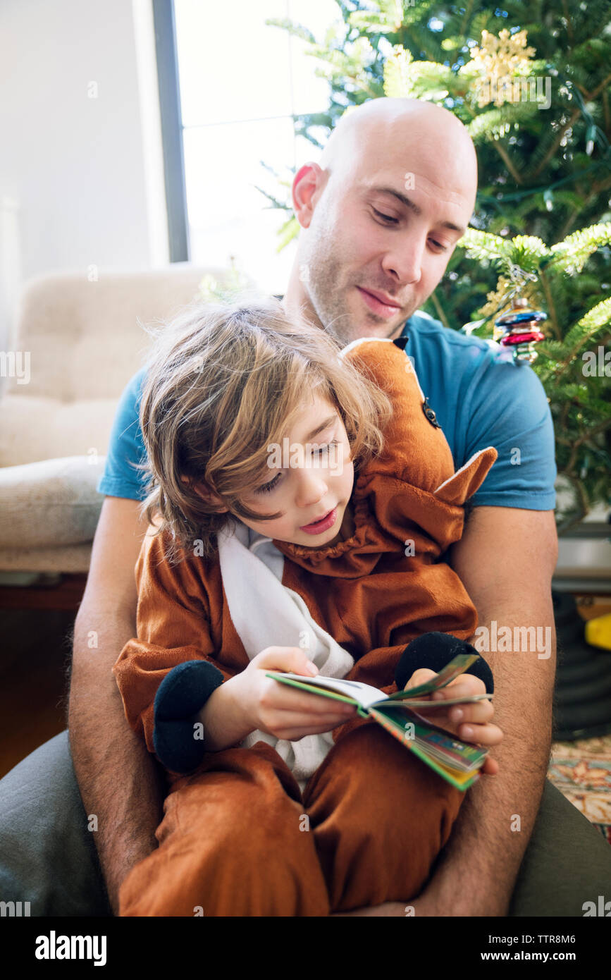 Father sitting with son dressed in costume against christmas tree at home Stock Photo