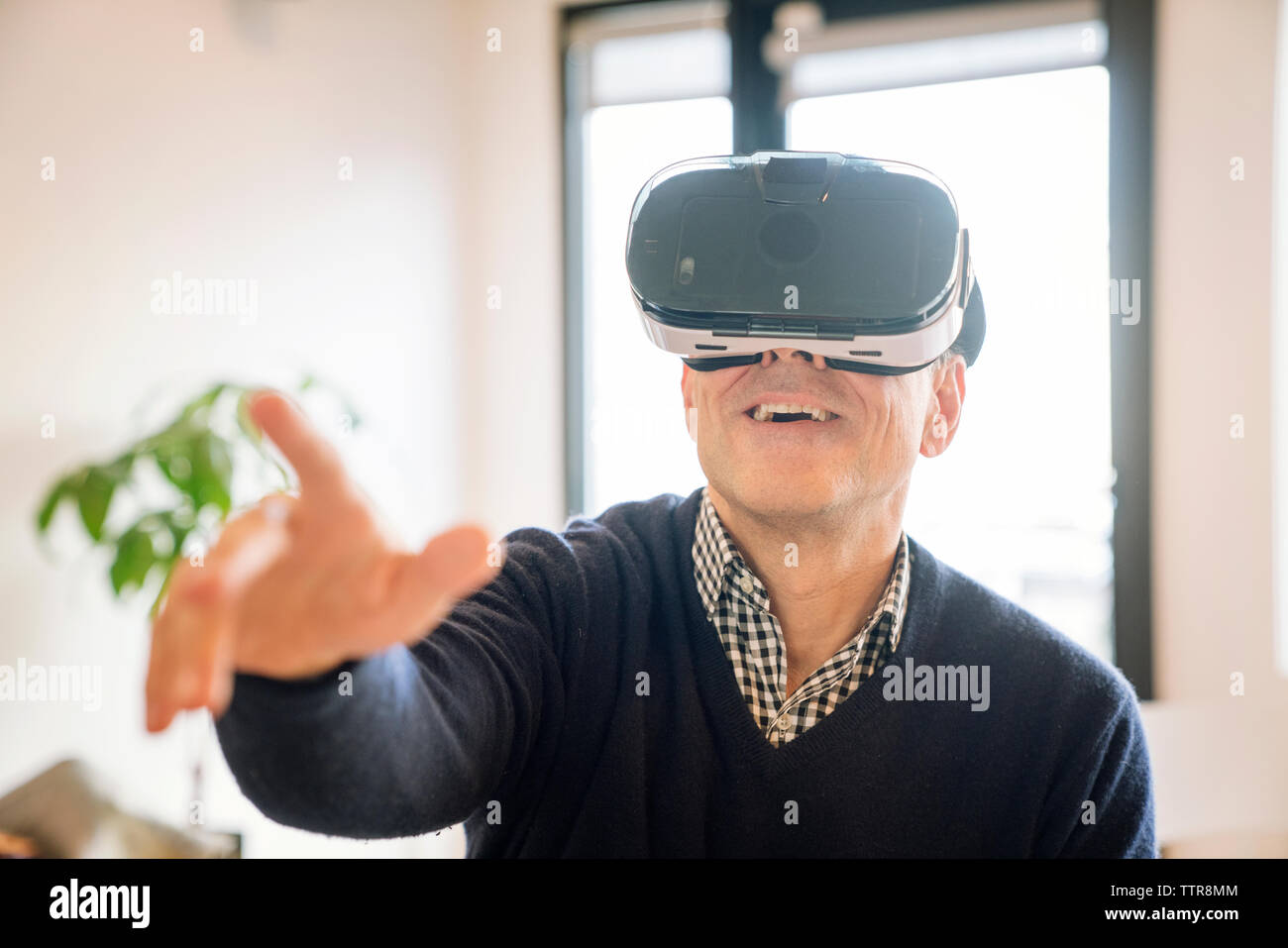 Smiling man pointing while wearing virtual reality simulator at home Stock Photo