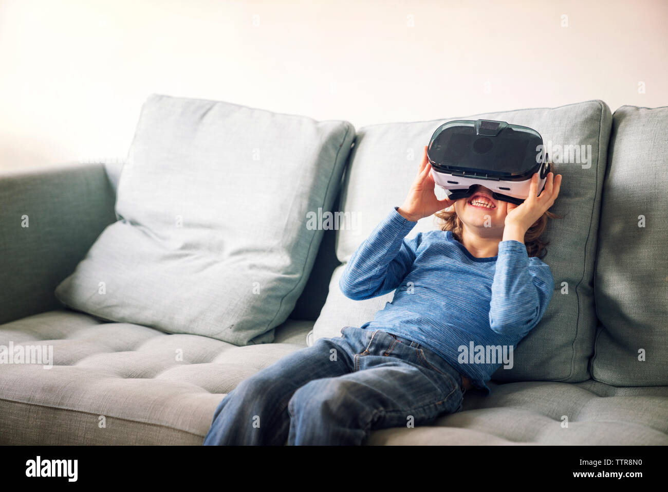 Happy boy wearing virtual reality simulator sitting on sofa at home Stock Photo