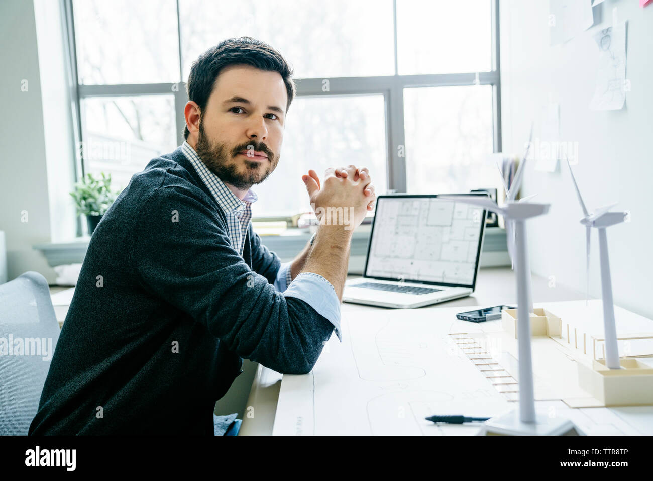 Portrait of businessman with hands clasped sitting at desk in office Stock Photo