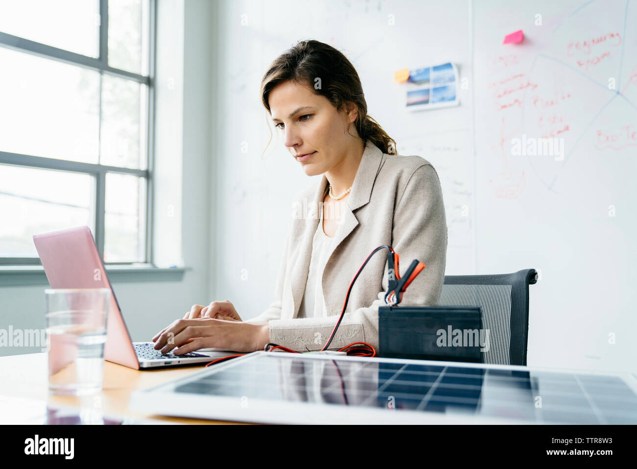 businesswoman using laptop computer while sitting against whiteboard in office Stock Photo