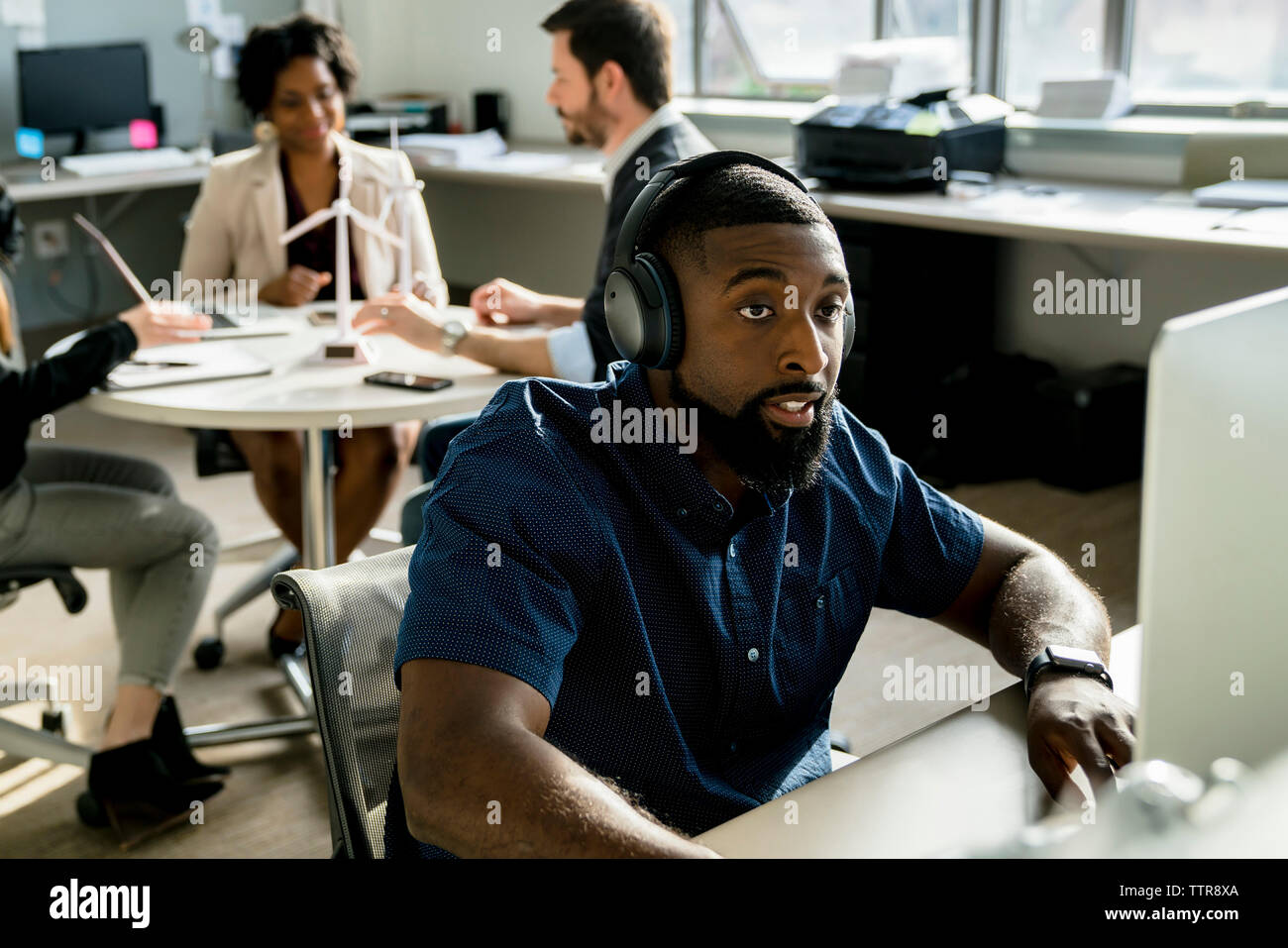 businessman using desktop computer while colleagues discussing in background Stock Photo