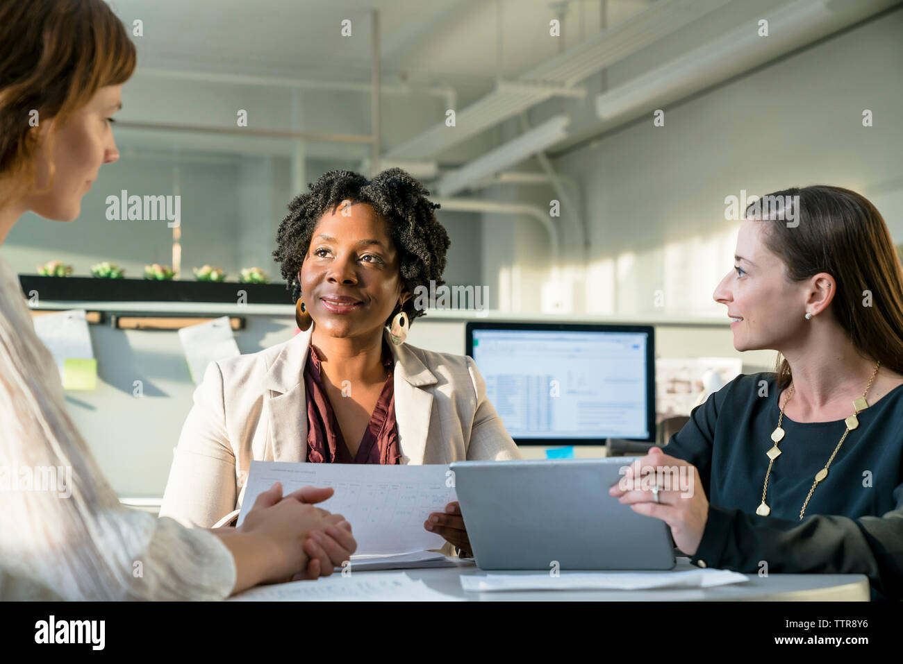Smiling businesswomen discussing over tablet computer while sitting in office Stock Photo