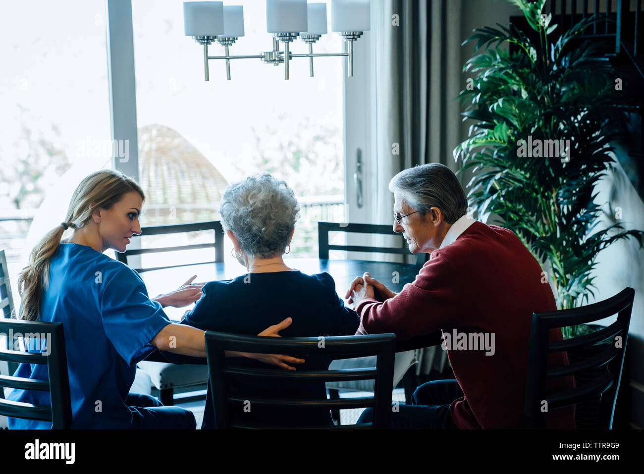 Home caregiver discussing with senior couple while sitting at dining table Stock Photo