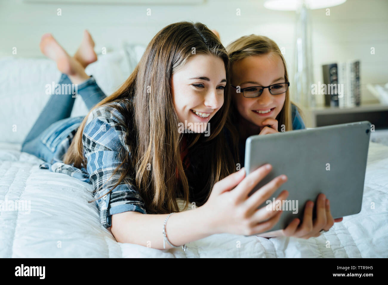 Happy sisters using tablet computer in bedroom Stock Photo - Alamy