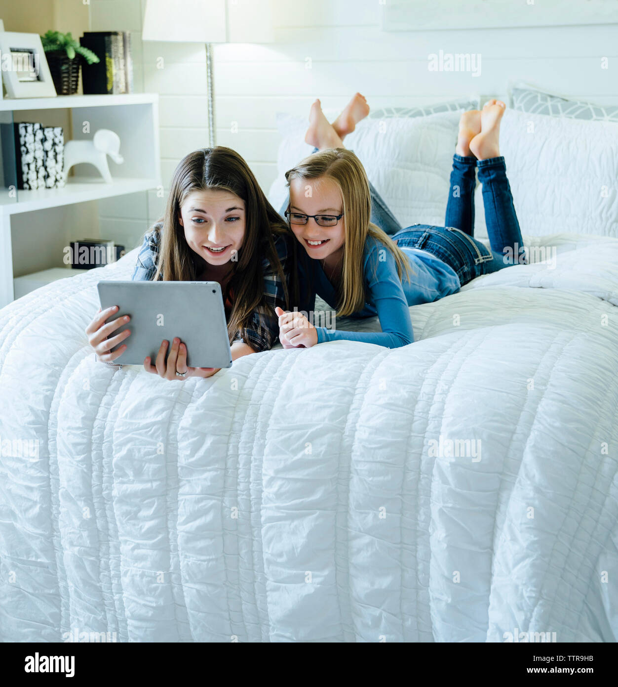 Sisters using tablet computer while lying on bed in bedroom Stock Photo Alamy