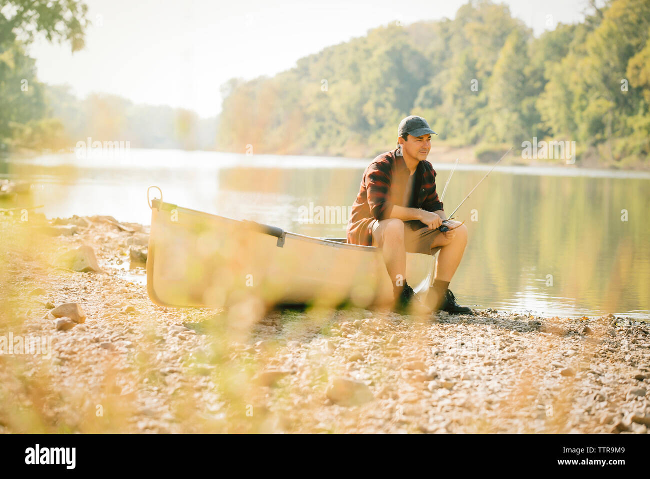 Mid adult man looking away while sitting on boat at lakeshore Stock Photo