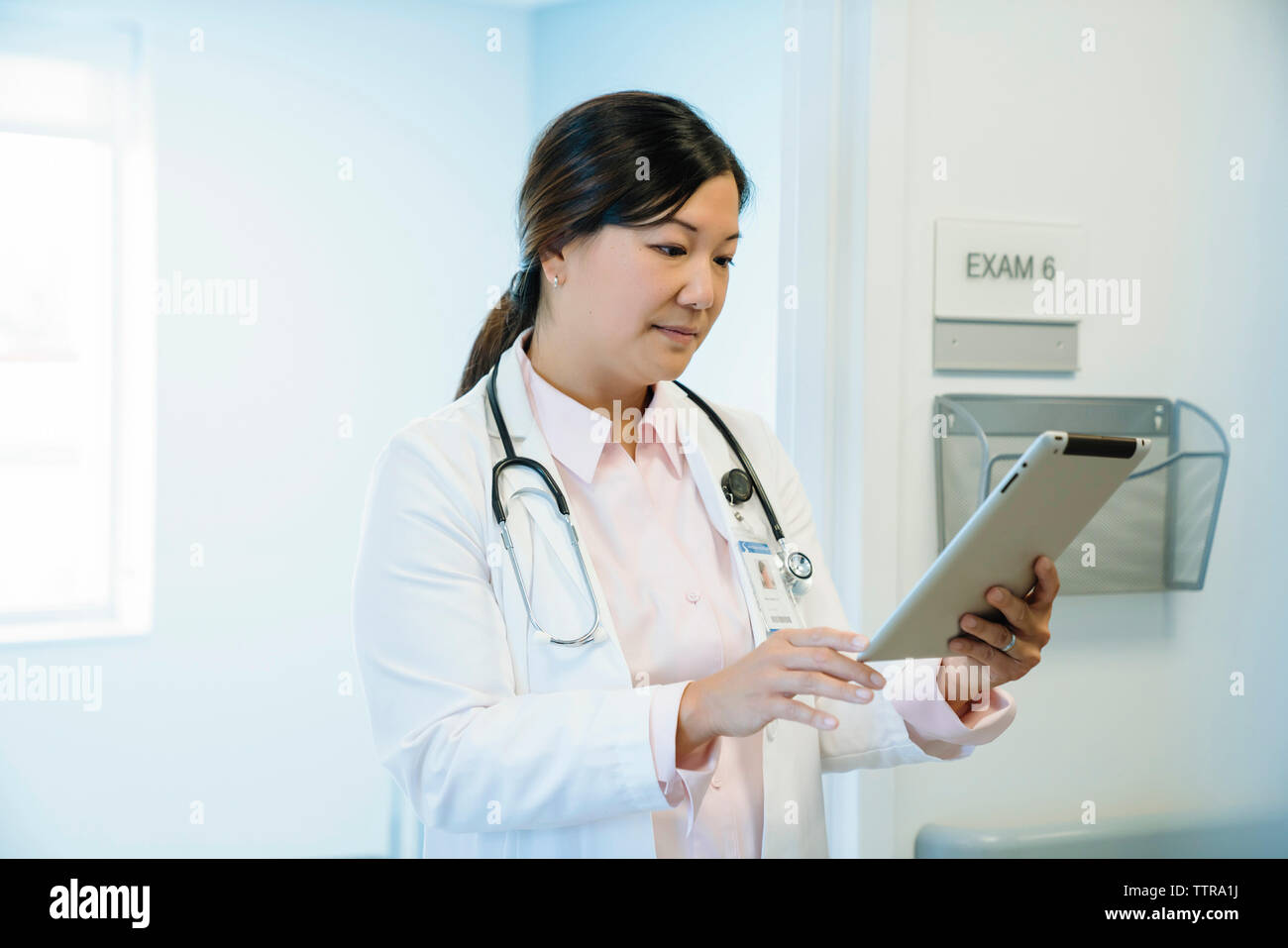 Female doctor looking at tablet computer while standing in hospital corridor Stock Photo