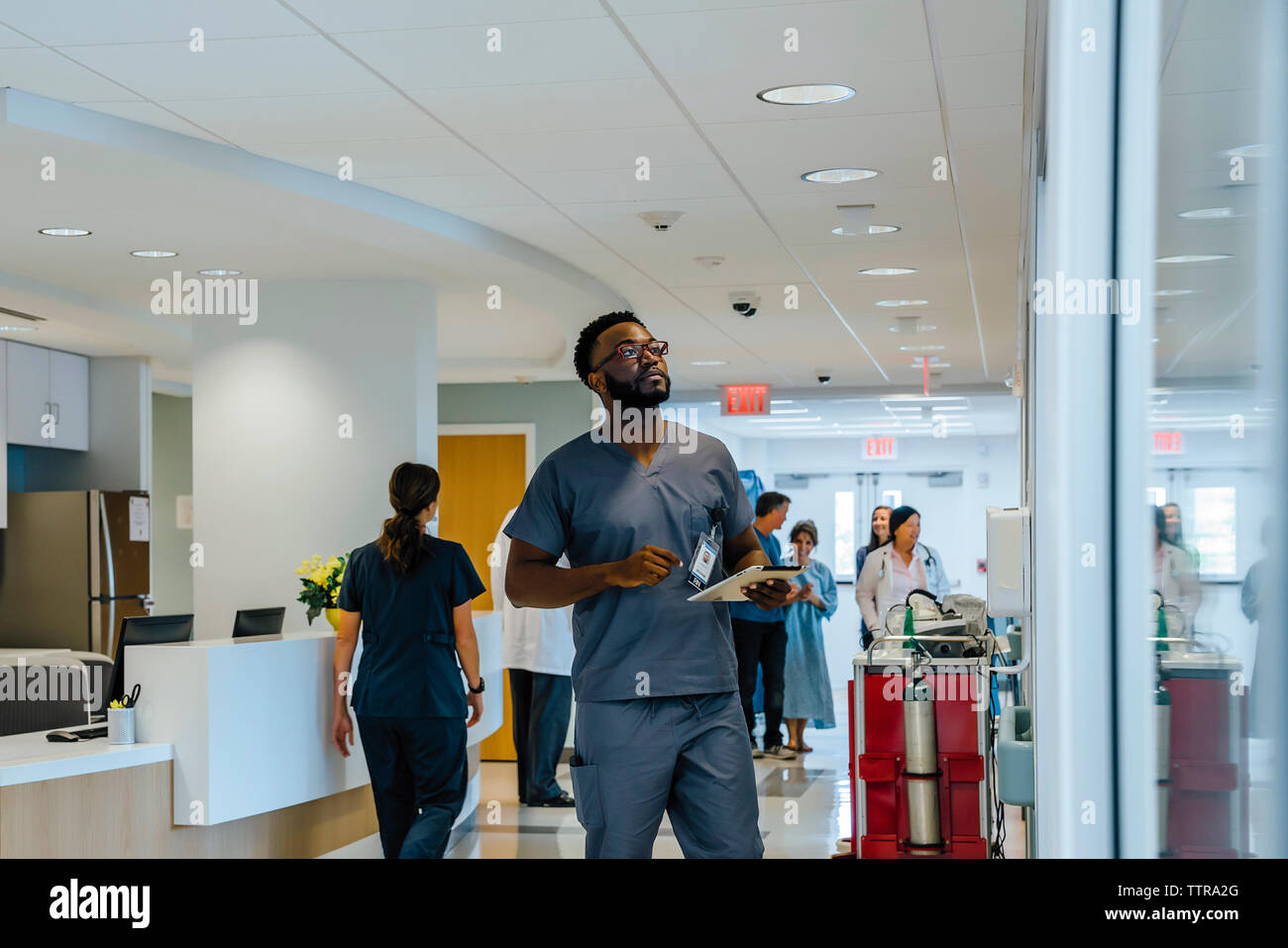 Doctor holding tablet computer while looking away with colleagues working in background Stock Photo