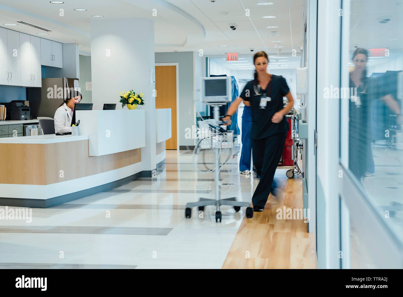 Female doctor working at reception while nurse taking monitoring equipment at hospital Stock Photo