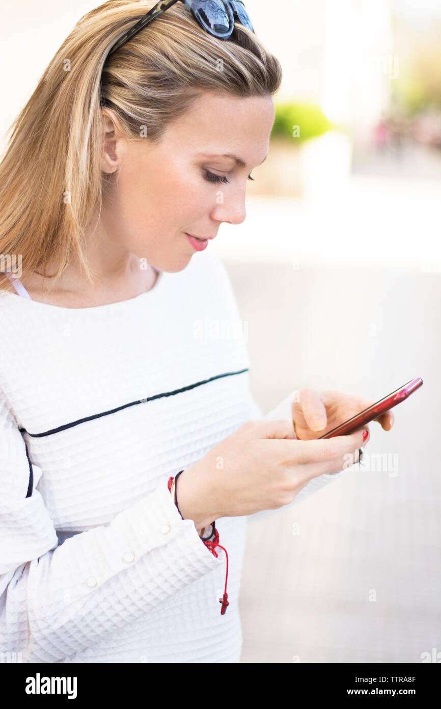 Woman using mobile phone while standing on footpath Stock Photo