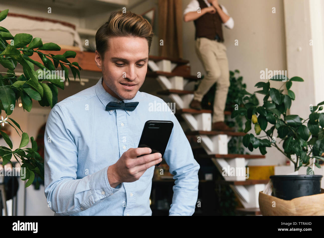 Gay Man Using Smart Phone While Boyfriend Walking Down Steps In Background At Home Stock Photo Alamy