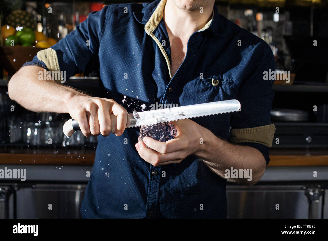 Midsection of chef cutting ice block in kitchen Stock Photo