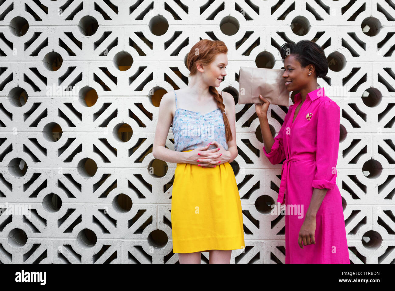 Multi-ethnic friends talking while standing against patterned wall Stock Photo
