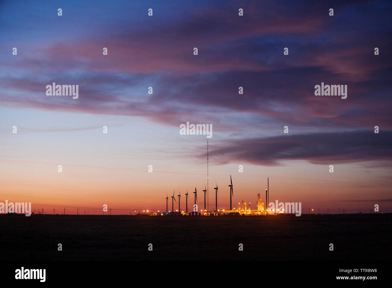 Illuminated power plant against cloudy sky at dusk Stock Photo